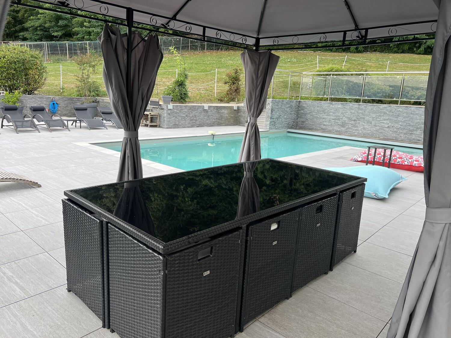 Grand salon de jardin abrité sous une tonnelle, face à la piscine chauffée