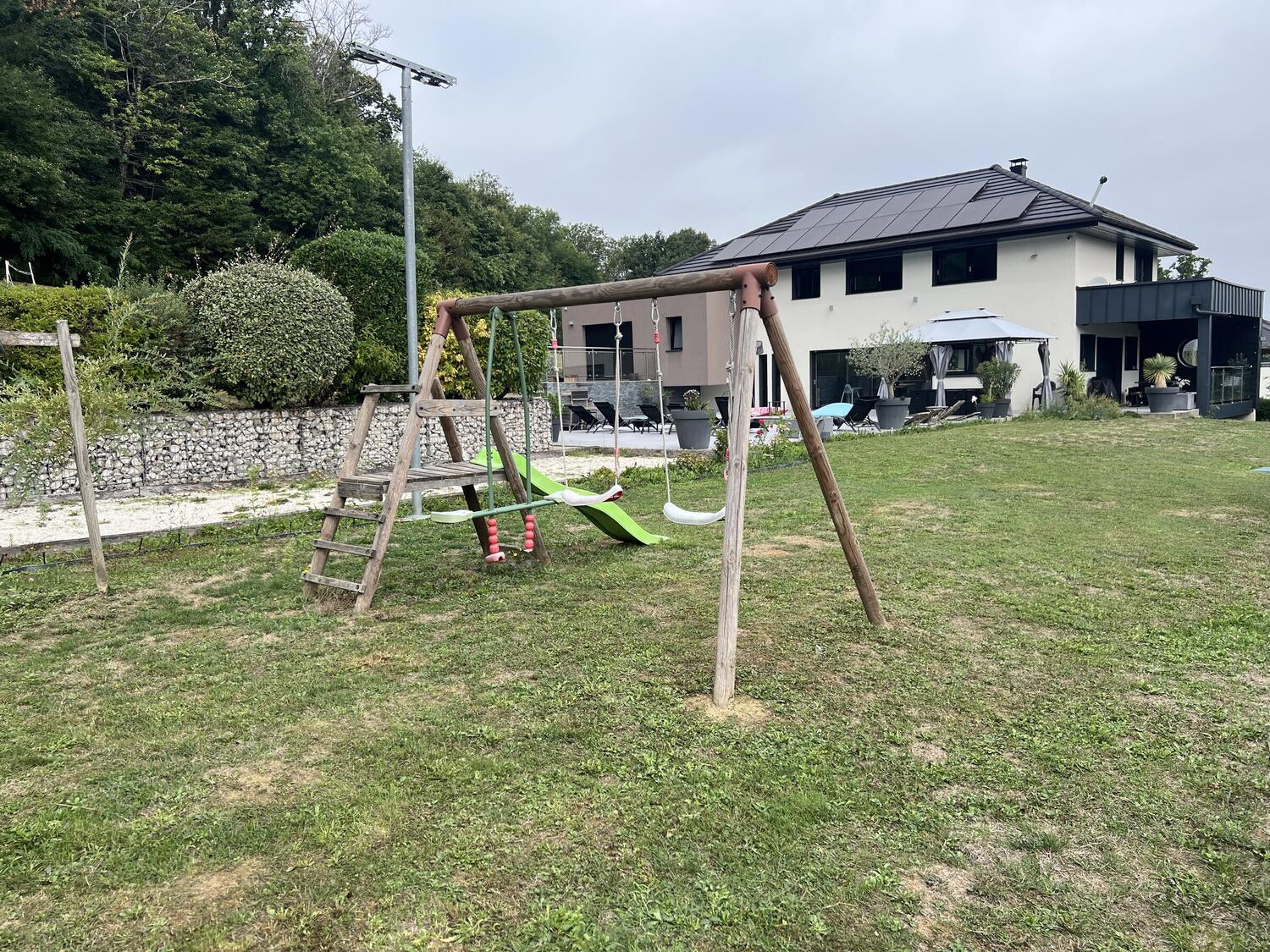 Aire de jeux avec portique, balançoires et toboggan dans le jardin clos de la villa